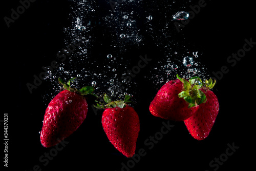 fresh strawberries falling into water leaving splashes
