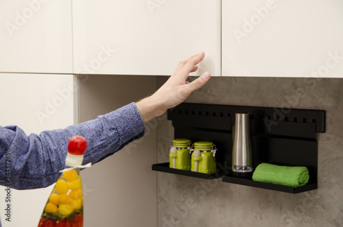man closes a cabinet without a handle in a modern kitchen