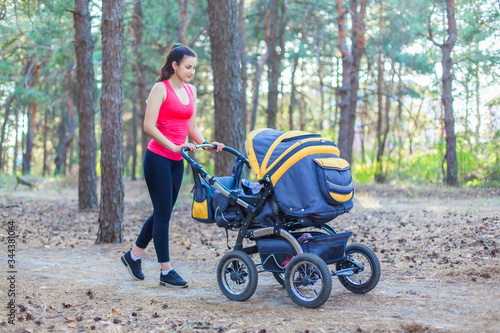 Nature walk with stroller, young active mother in sportswear walking on the forest walkway with her baby in the pram, enjoying fresh air © satyrenko