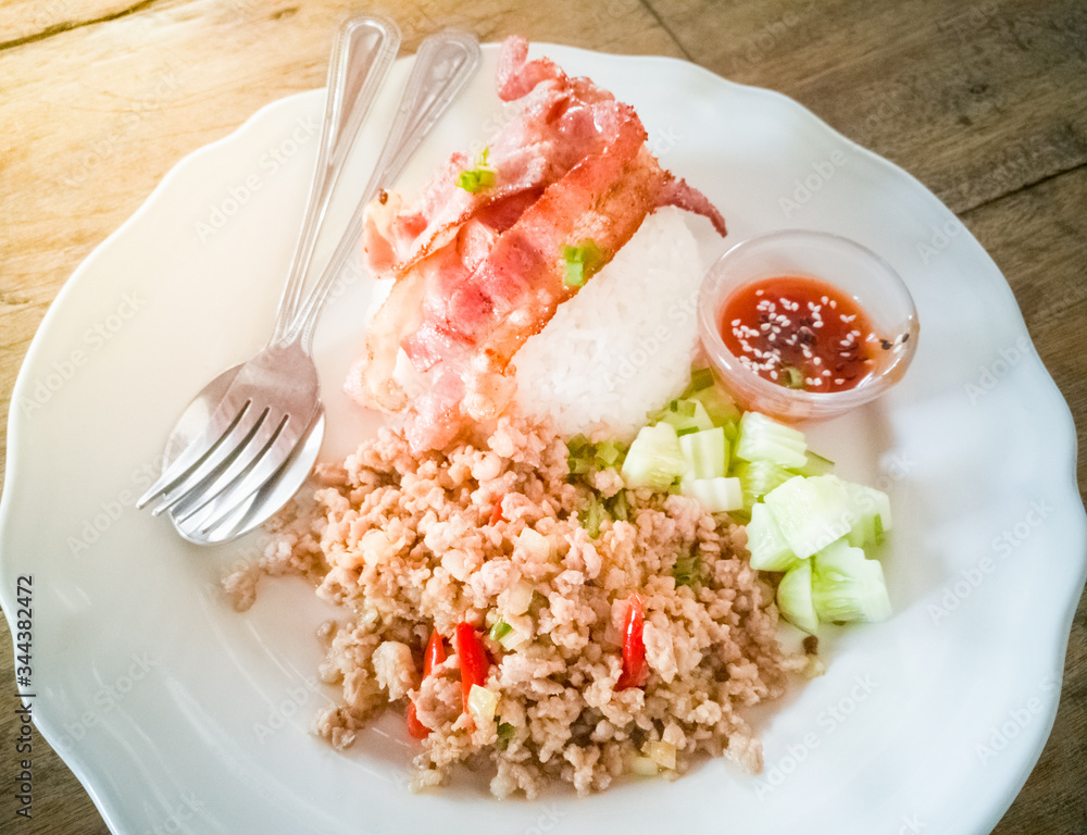 Stir fried minced pork and bacon, fried on rice and cucumber on a white plate on the table Stir fried minced pork and bacon, fried on rice and cucumber on a white plate on the table