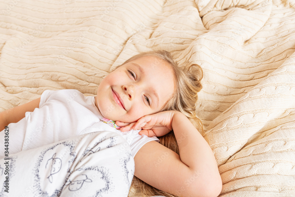 Beautiful little girl in pajamas lying on the bed at home. Stay at home during coronavirus covid-19 lockdown and have a fun. Happy childhood concept Beautiful little girl in pajamas lying on the bed at home. Stay at home during coronavirus covid-19 lockdown and have a fun. Happy childhood concept