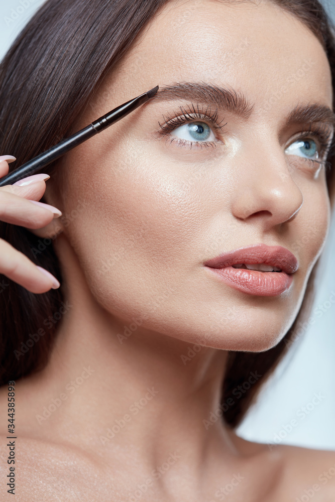 Fototapeta premium Eyebrows Makeup. Woman Shaping Brow With Cosmetic Brush. Beautiful Girl Close Up Portrait. Brunette With Perfect Skin And Blue Eyes.