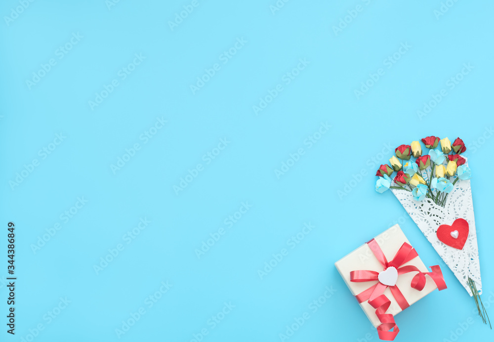 The bouquet of craft flowers wrapped in a white lace bundle and gift box with red ribbon on blue background. Mother day, Valentine day, Wedding, Birthday concept. Greeting card. Flat lay style. The bouquet of craft flowers wrapped in a white lace bundle and gift box with red ribbon on blue background. Mother day, Valentine day, Wedding, Birthday concept. Greeting card. Flat lay style.