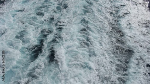 Water boils and foams from the propellers of the ship, this trail stretches far into the distance to the sea.