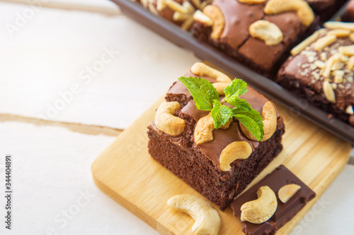 Chocolate brownies with cashew nut and peppermint on wooden plate on white wooden floor with brownies box blurred background.