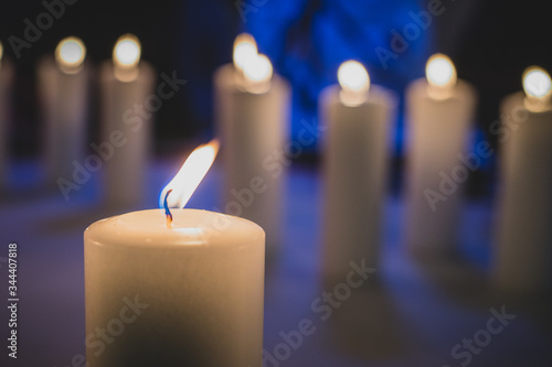 Detail of a white candle being lit up, with a row of other candles in the background. Blue backlight seen in the background.
