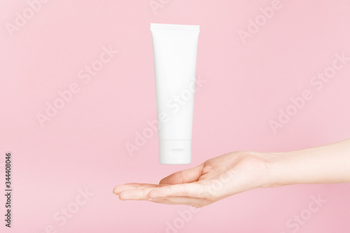 Female hand holding flacon for cream with golden cap. Plastic flacon for body lotion, toiletry. Container for cosmetics product. Skincare, advertising concept. Mockup style. Isolated on pink © mellisandra