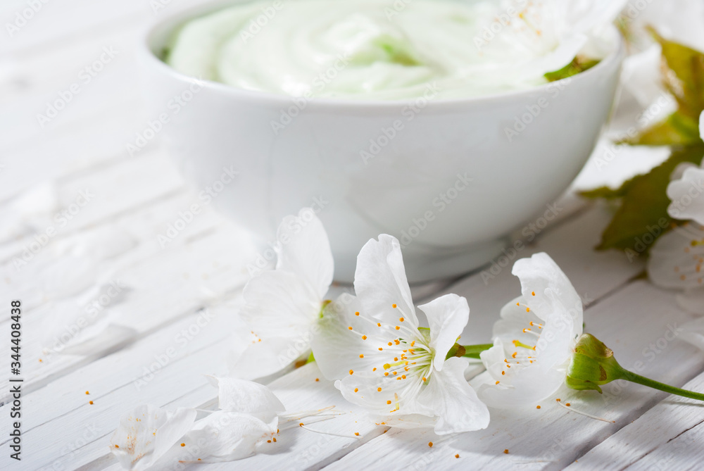 moisturizer cream with cherry blossom on white wooden table background