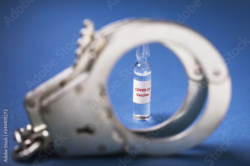 Ampoule with covid-19 pandemic vaccine and handcuffs on a blue background. Coronavirus drug fraud punishment concept photo