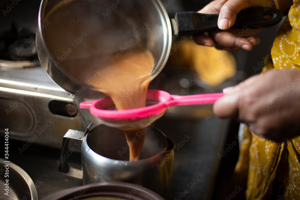 Tea being strained and poured into the cups from a steel tea pot in an Indian kitchen. Indian drink and beverages. Tea being strained and poured into the cups from a steel tea pot in an Indian kitchen. Indian drink and beverages.