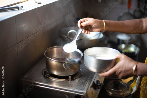 Tea being strained and poured into the cups from a steel tea pot in an Indian kitchen. Indian drink and beverages.