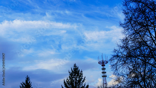 Big television and radio tower and trees on the classic blue sky background. Space for text.