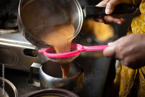 Tea being strained and poured into the cups from a steel tea pot in an Indian kitchen. Indian drink and beverages. © abir