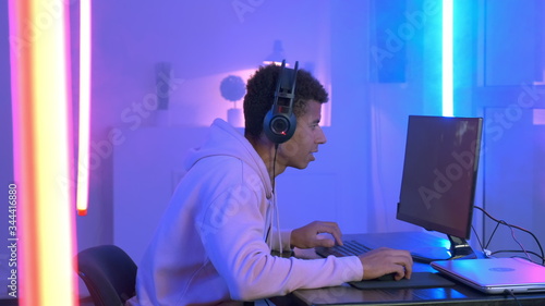 Photos Profile view of young gammer in headphones playing in online shooter