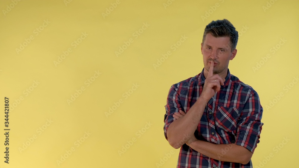 On yellow background cheerful tall boy making a hush gesture. It must be quite there.