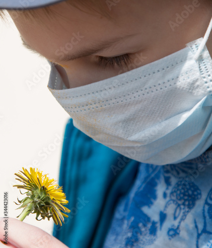 boy sniffing a dandelion in a protective medical mask photo