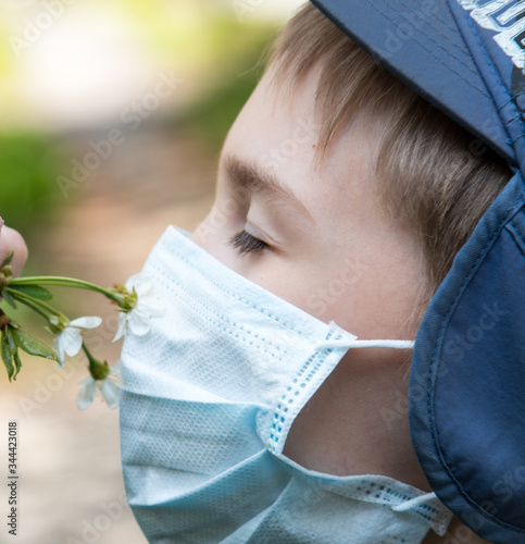 boy sniffs cherry tree flowers in a protective medical mask photo