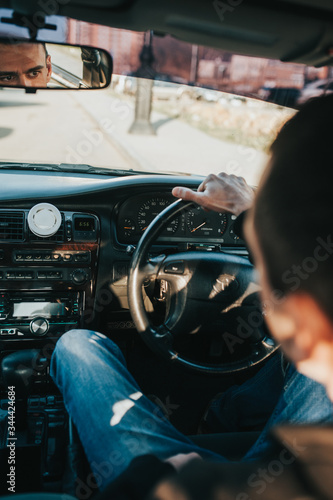 a tough brutal man in black clothes holds the steering wheel of a Toyota Mark 2 car and looks with big brown eyes in the rearview mirror