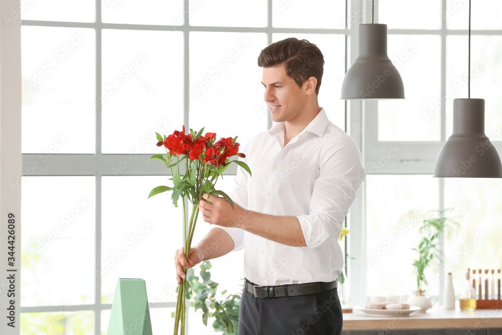 Handsome man putting bouquet of flowers in vase indoors Handsome man putting bouquet of flowers in vase indoors