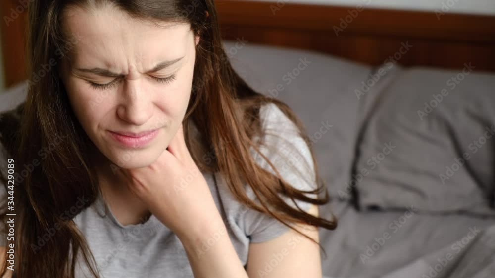 Unhealthy young woman touch neck hard to swallow having discomfort or painful feeling sitting on bed at home, unwell sad girl suffering from angina, sore throat, experience loss of voice Unhealthy young woman touch neck hard to swallow having discomfort or painful feeling sitting on bed at home, unwell sad girl suffering from angina, sore throat, experience loss of voice