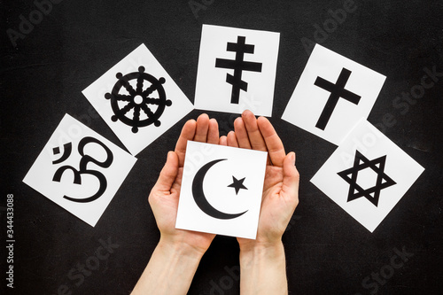 Choose religion concept. Hand with Islam crecent near world religions symbols on black background top view photo