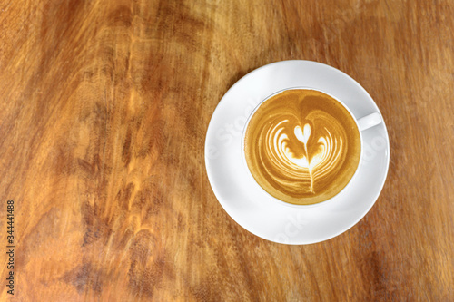 Hot latte coffee in white ceramic cup and saucer placed on wood table with copy space (Top view)