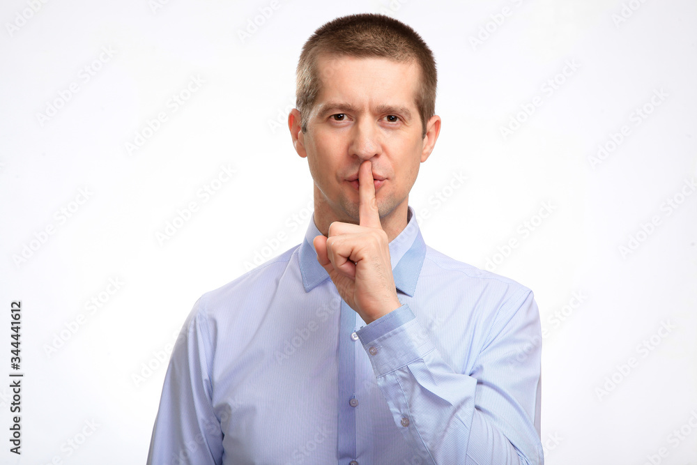 Φωτογραφία successful businessman put his index finger to his lips, calling for a secret, showing a sign of silence, in a blue light casual shirt, a glance at the camera