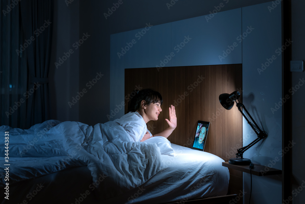 Fototapeta premium Asian woman virtual happy hour meeting online together with her boyfriend in video conference to good night before sleep at night with digital tablet for a online meeting in video call