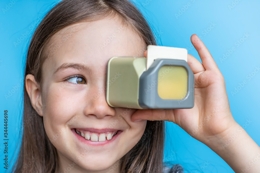 Smiling child girl looks at old photos through a diascope. Banner template on blue background. Smiling child girl looks at old photos through a diascope. Banner template on blue background.