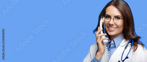 Portrait picture of happy smiling young doctor talking on phone, against blue background. Copy space for some sign, slogan or advertising text. Medical call center service. photo