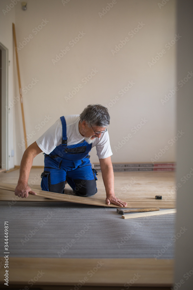 DIY, repair, building and home concept - Senior landlord lying parquet floor board/laminate flooring in a rental appartement (shallow DOF; color toned image) DIY, repair, building and home concept - Senior landlord lying parquet floor board/laminate flooring in a rental appartement (shallow DOF; color toned image)