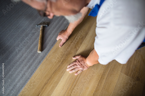 DIY, repair, building and home concept - close up of male hands lying parquet floor board/laminate flooring (shallow DOF; color toned image)