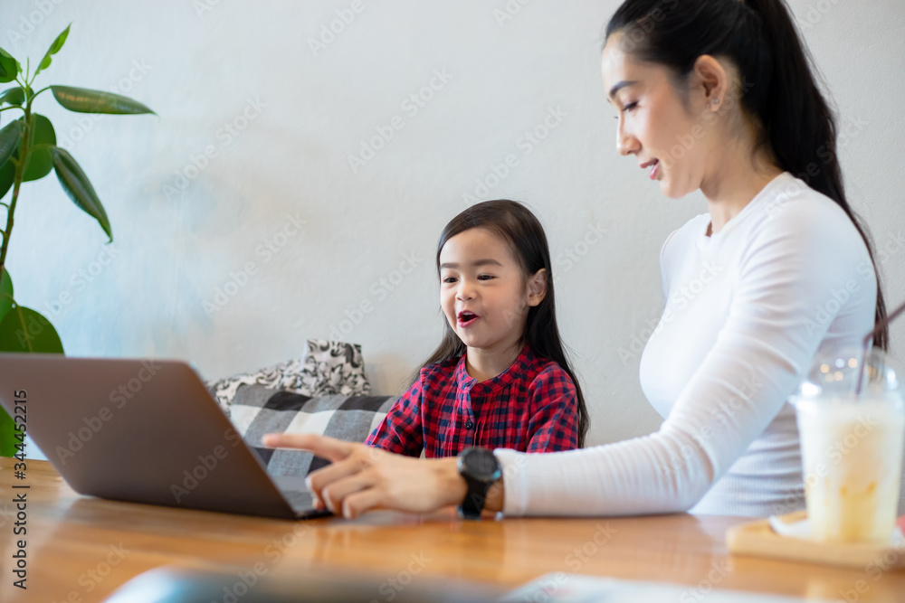 Asian mothers are teaching their daughters to read a book and use notebooks and technology for online learning during school holidays at home. Educational concepts and activities of the family Asian mothers are teaching their daughters to read a book and use notebooks and technology for online learning during school holidays at home. Educational concepts and activities of the family