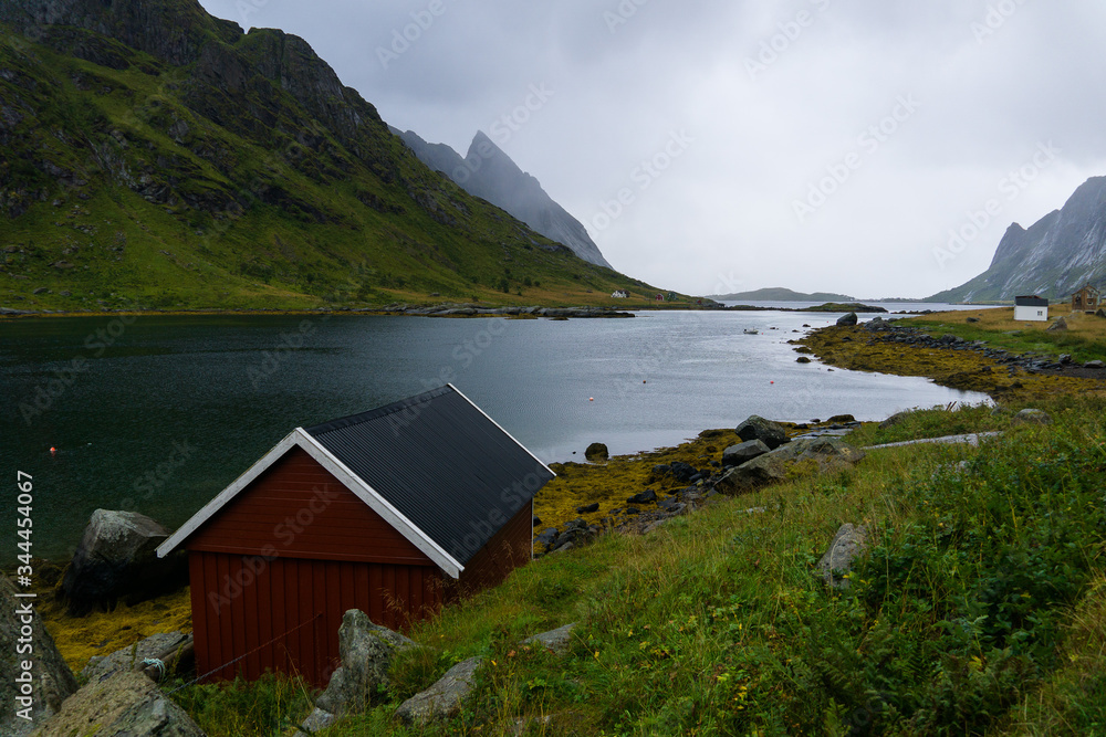 Lonely red hut on the shore of Reinefjorden in a rainy day in Lofoten islands of Norway
