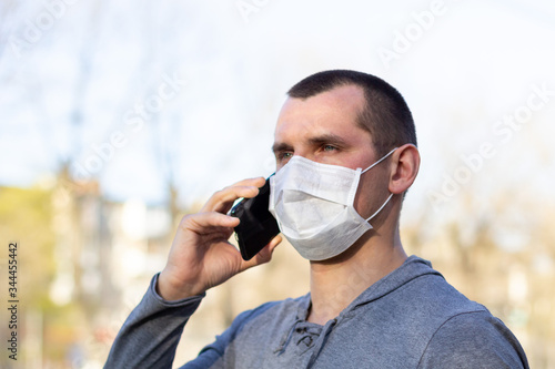 Caucasian man in medical mask on his face calling by phone. protected from virus in street outdoor.