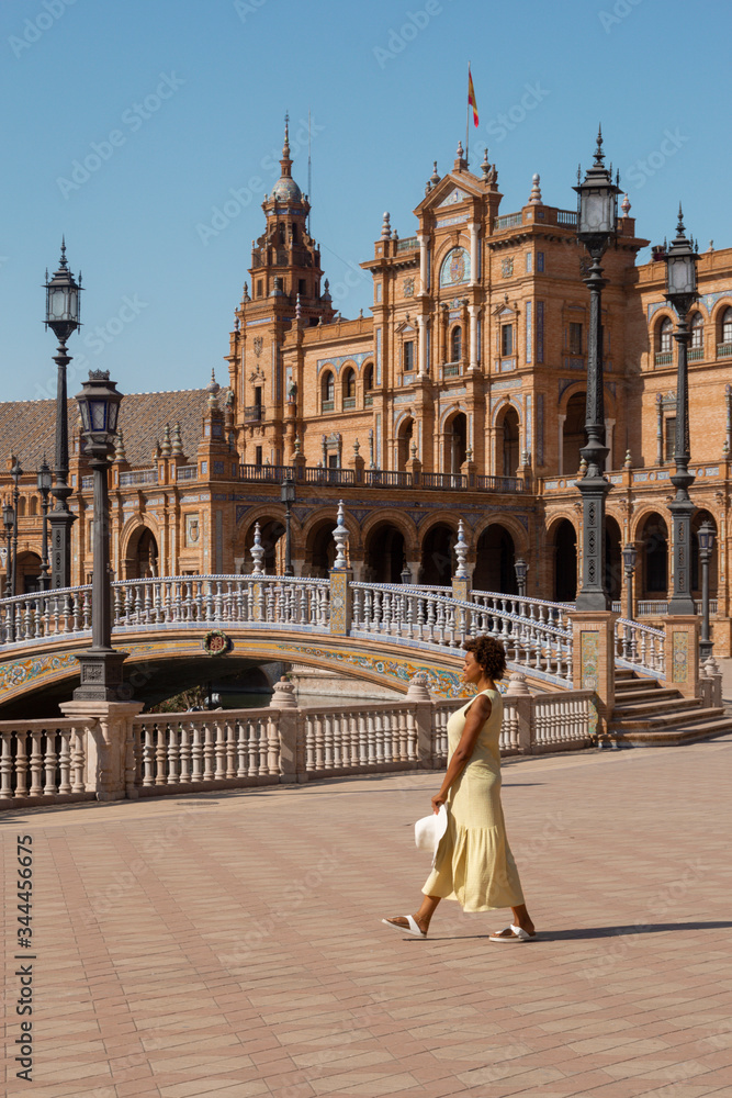 Fototapeta premium afro american woman in plaza españa, sevilla. girl wearing a yellow dress and white hat