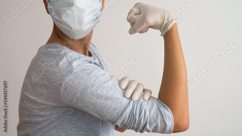 Woman doctor with a surgical mask and white rubber gloves in position of Rosie the Riveter "We Can Do It!" 