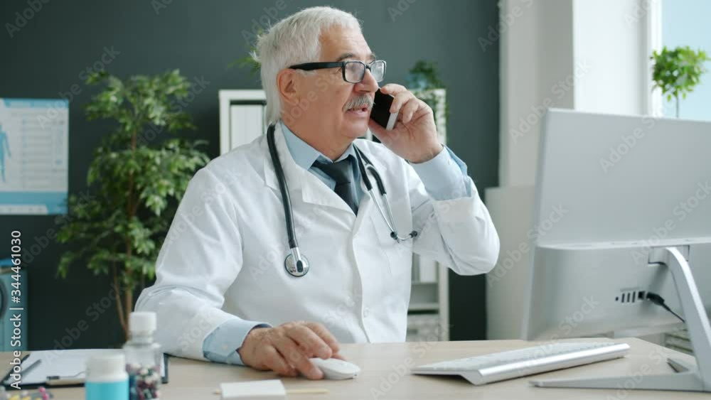 Medical specialist talking to patient on mobile phone and using pc working in office in contamporary hospital. Communication and technology concept. Medical specialist talking to patient on mobile phone and using pc working in office in contamporary hospital. Communication and technology concept.