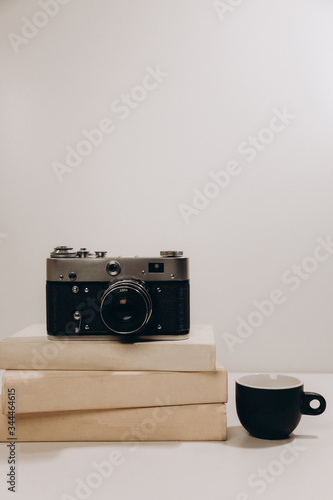 Black cup of coffee with old vintage camera and white books on gray isolated background