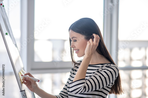 Dark-haired girl in a striped shirt writin on a flipchart photo