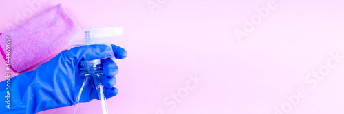 Female hand in blue rubber gHands in rubber protective gloves holding white spray bottle and rag. Detergent for different surfaces in kitchen, bathroom and other rooms. Closeup. Light pastel pink back photo