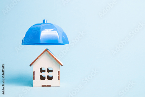 blue plastic umbrella over wooden model of a house, blue background copy space, insurance and real estate protection concept.