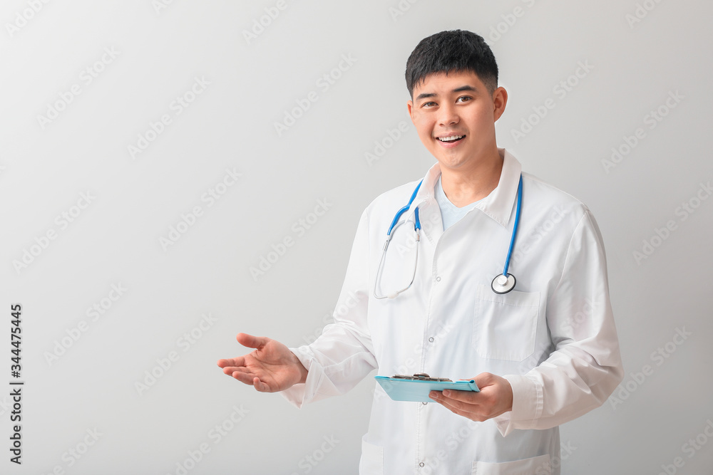 Male Asian doctor showing something on light background Male Asian doctor showing something on light background
