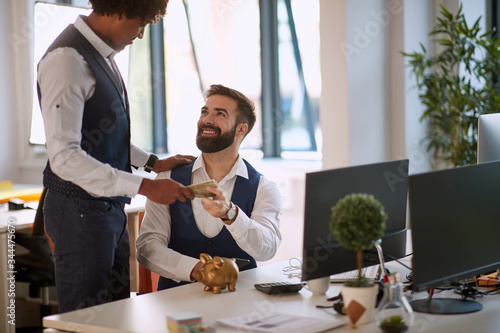 Afro-american gives to a Caucasian male cash from hand to hand in office. loan, bribe concept photo