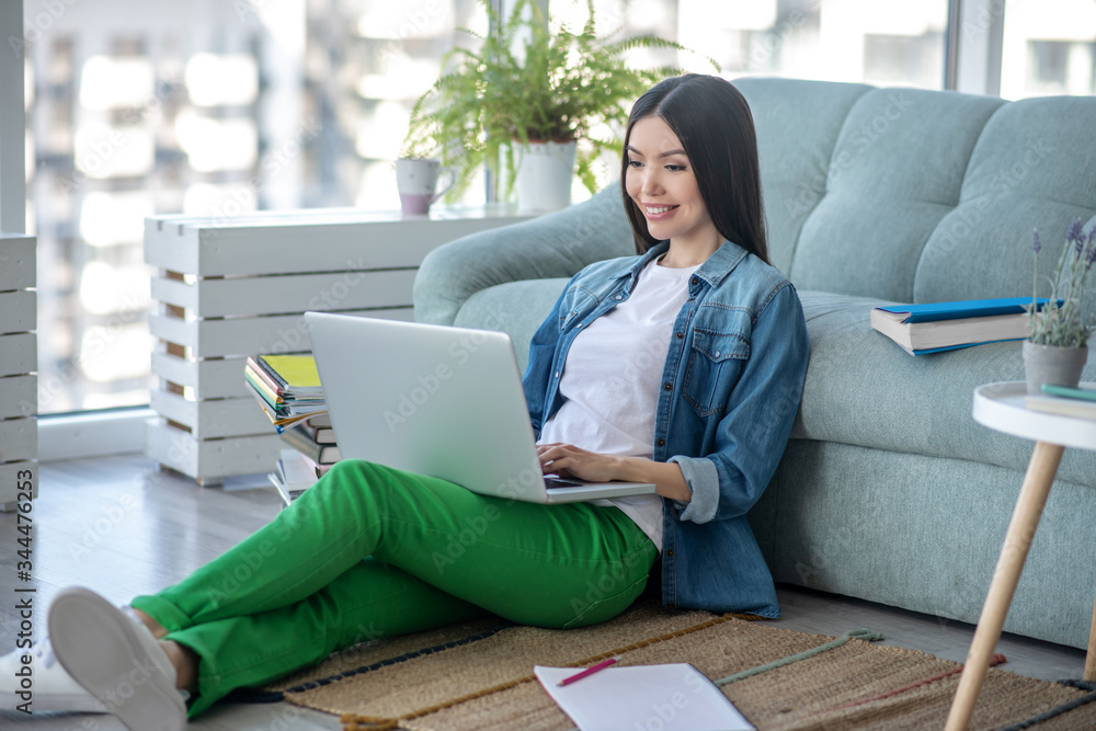 Young woman in green pants sitting on the floor and chatting in internet Young woman in green pants sitting on the floor and chatting in internet