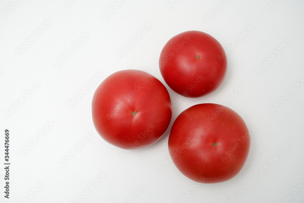 Tomato on white background. Three tomatoes placed on a white desktop Tomato on white background. Three tomatoes placed on a white desktop
