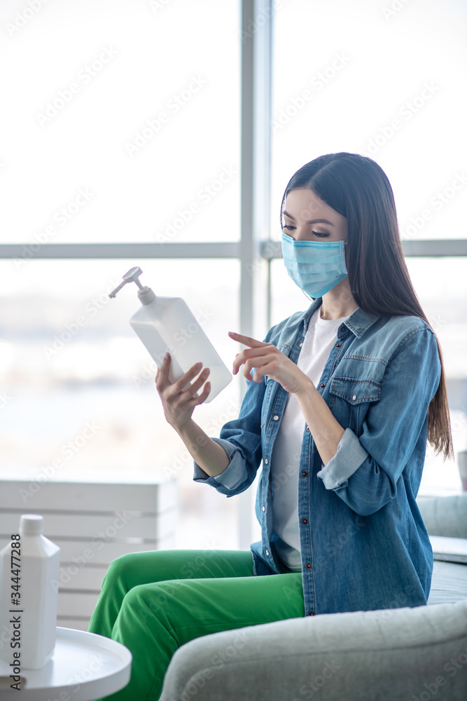 Fototapeta premium Young woman in a protective mask holding a bottle with sanitizer