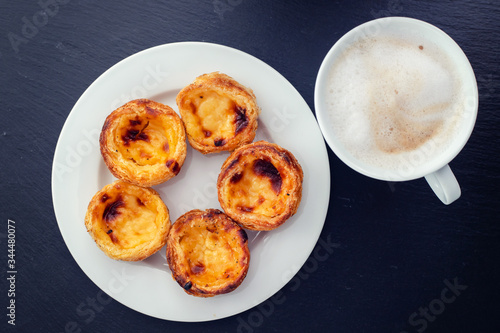 portuguese egg tart pastel de nata on white plate and cup of coffee with milk