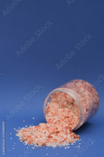 Pink sea salt in a clear jar was scattered on a dark blue background. Isolated. Free space for text 