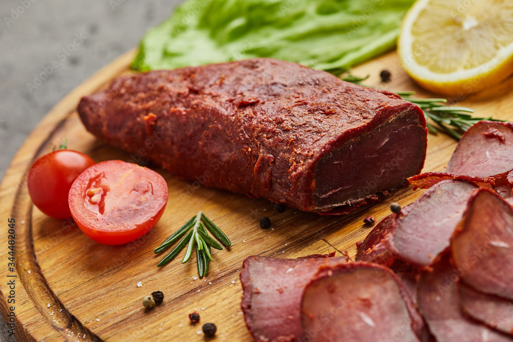 Armenian basturma or Pastirma on wooden cutting board decorated with spices, lettuce, lemon and tomatoes. Meat smoked jerky good as Beer snack Armenian basturma or Pastirma on wooden cutting board decorated with spices, lettuce, lemon and tomatoes. Meat smoked jerky good as Beer snack